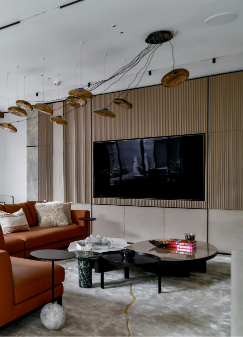 Luxury modern living room with a wall-mounted flat-screen TV, wood slat accent wall, sculptural ceiling lights, and rust-colored sofas.